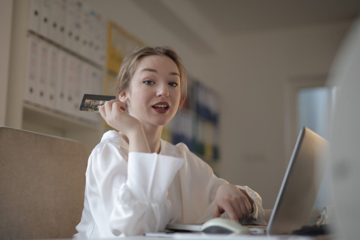 A woman holding a card while working on a laptop