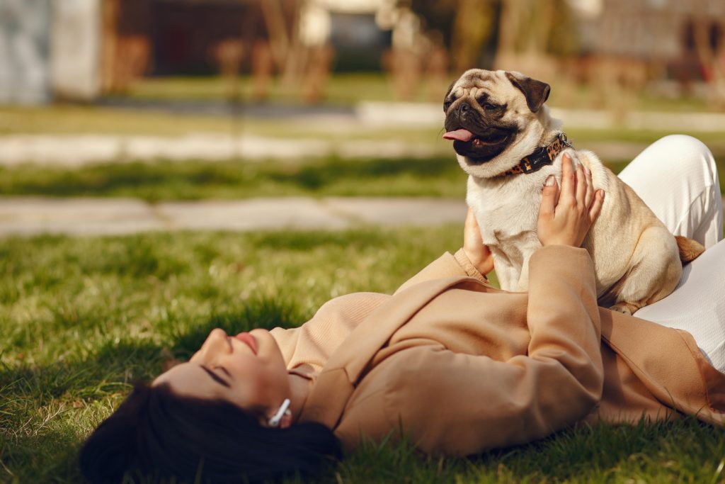 A woman laying on a grassy lawn with her dog on her stomach