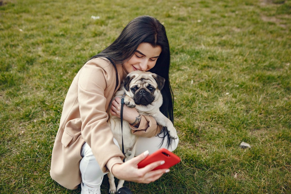 Picture of a woman taking selfie with her dog on a lawn